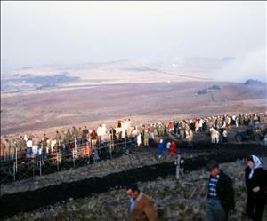 Crowds of people standing and sitting in bleachers on a grassy hill on a foggy day